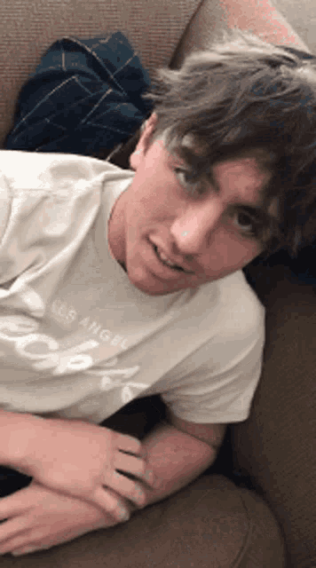 a young man laying on a couch wearing a los angeles t-shirt