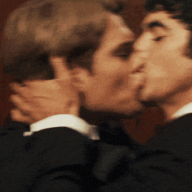 a man in a suit kissing another man on the cheek