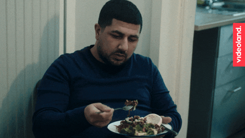 a man in a blue shirt is eating a salad with a videoland logo in the background