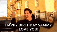 a man is standing in front of a building with his arms in the air and says `` happy birthday sammy love you ! ''