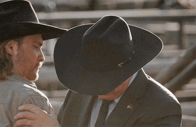 a man wearing a cowboy hat and a man in a suit hugging each other