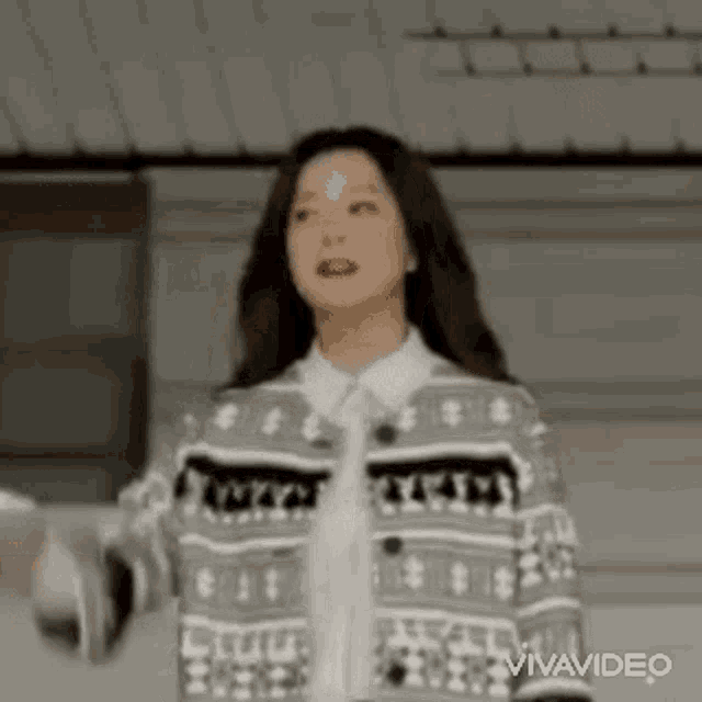 a woman wearing a sweater and a white shirt is standing in a room with her arms outstretched .