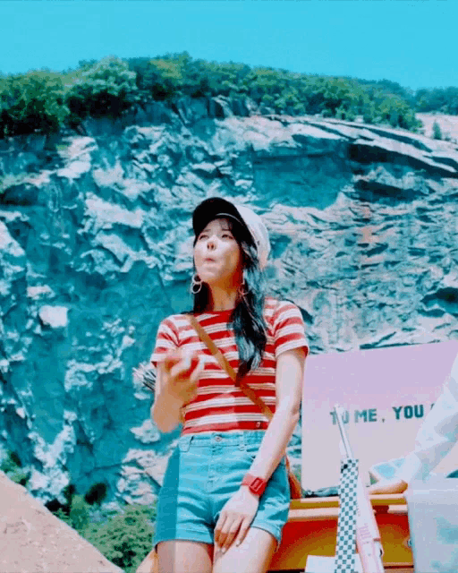 a woman wearing a striped shirt and shorts is holding an apple in front of a sign that says you me you