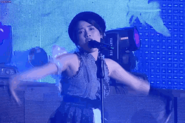 a woman is singing into a microphone on a stage in front of a large screen .