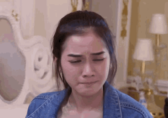 a woman in a denim jacket is crying in front of a mirror in a bedroom .