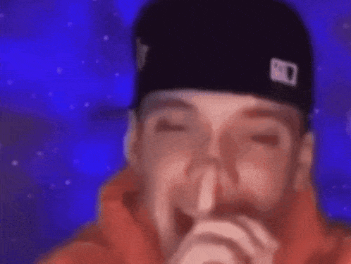 a close up of a man wearing a hat and covering his mouth with his hand .