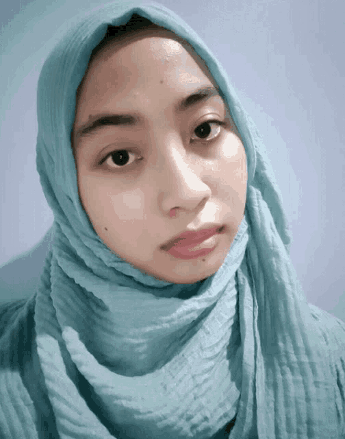 a woman wearing a blue scarf around her head looks at the camera