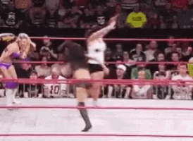 two women are wrestling in a ring while a crowd watches .