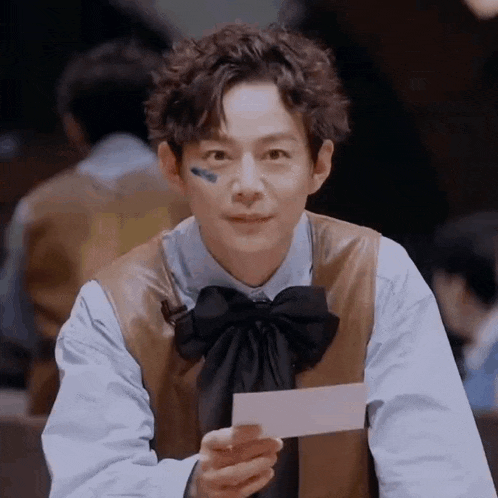 a man wearing a bow tie is holding a piece of paper in his hand .