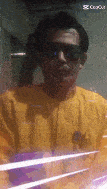 a man wearing sunglasses and a yellow shirt has a capcut watermark on the bottom right