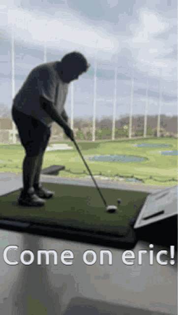 a man is swinging a golf club at a golf ball on a green mat .