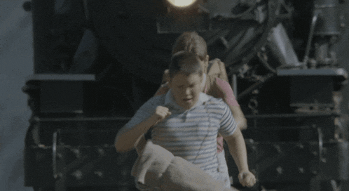 a boy and a girl are running in front of a black train
