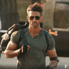 a man wearing sunglasses and a green shirt is carrying a backpack .