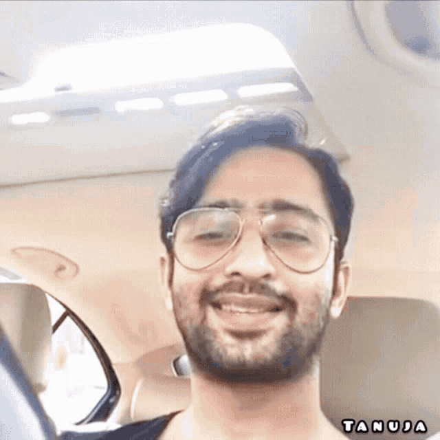 a man wearing glasses is sitting in a car and the name tanuja is on the bottom