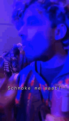a man with curly hair is smoking a cigarette in a dark room with a purple background .