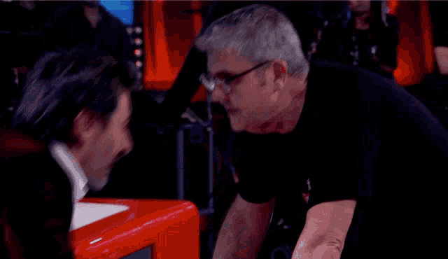 a man wearing glasses talks to another man in a black shirt