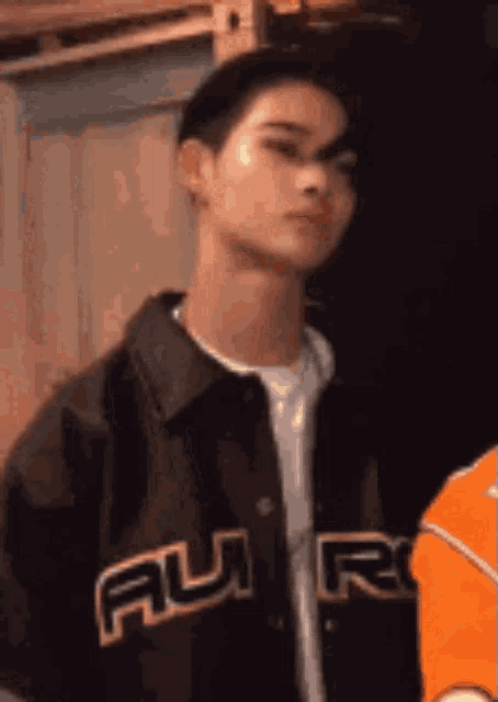 a young man wearing a black jacket and an orange shirt is standing in a room .