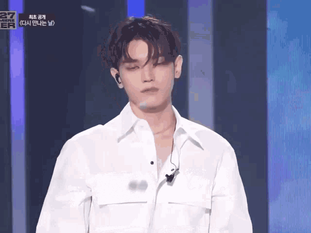 a young man wearing a white shirt and earphones stands in front of a sign that says 27 on it