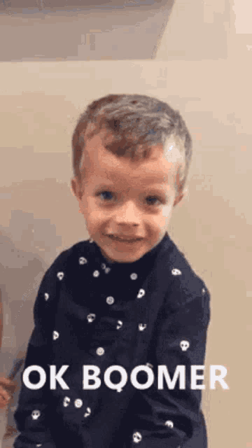a young boy wearing a blue shirt with skulls on it is standing in front of a wall .