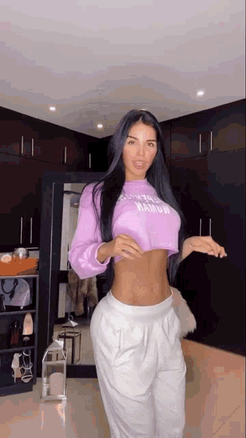 a woman is standing in front of a mirror wearing a purple crop top and white sweatpants .