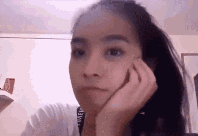 a young woman is making a funny face with her hand on her chin .