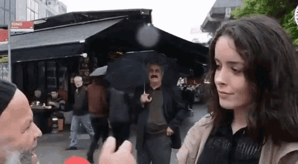 a man is holding an umbrella while talking to a woman on a city street .