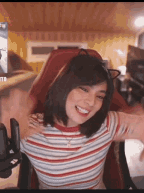 a woman in a striped shirt is sitting in a red chair with her arms outstretched and smiling .
