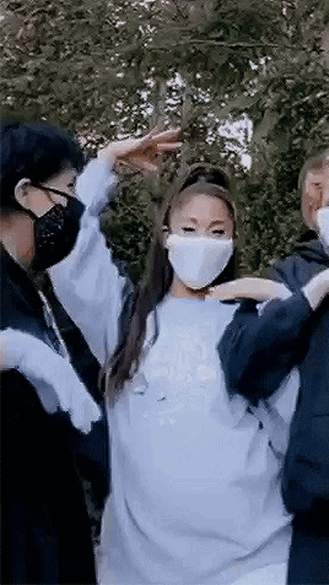 ariana grande is wearing a face mask and a sweatshirt while dancing with two people .