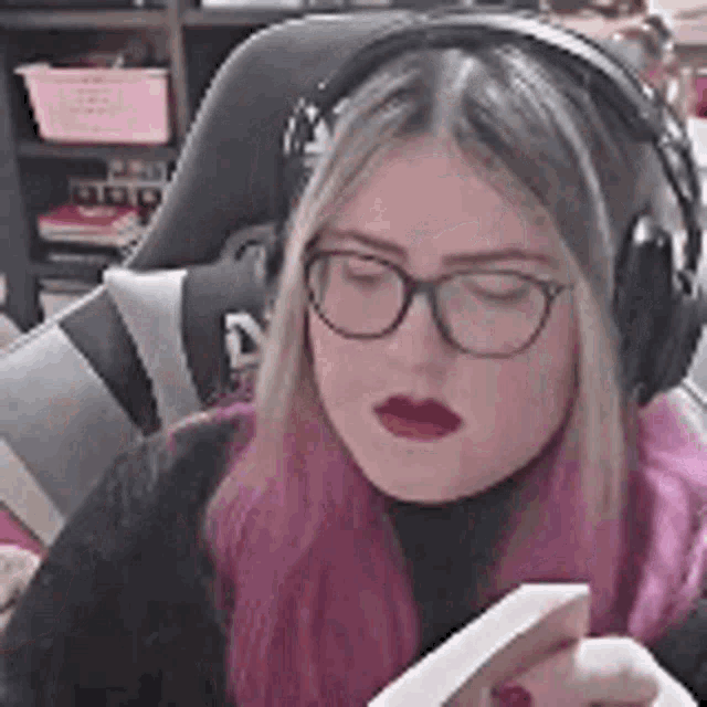 a woman wearing headphones and glasses is sitting in a chair reading a book .
