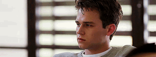 a young man is sitting in front of a window and looking away from the camera .