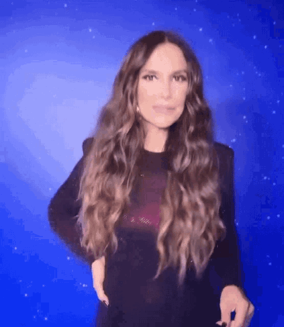 a woman with long hair is standing in front of a blue background and making a funny face .