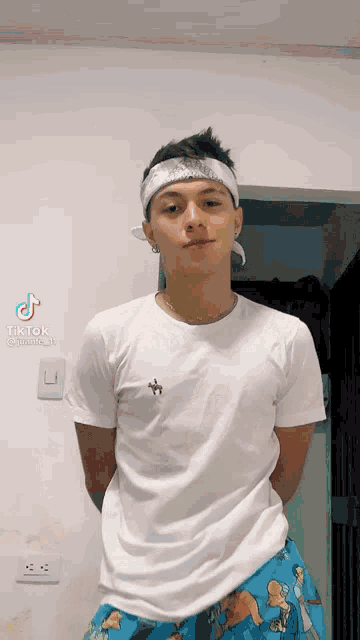 a young man wearing a white t-shirt and blue shorts is standing in front of a wall