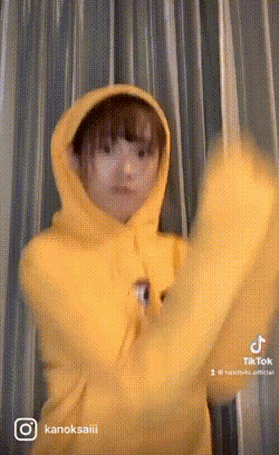 a woman wearing a yellow hoodie is standing in front of a curtain .