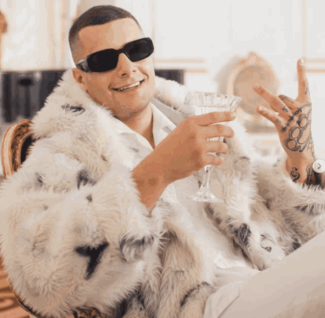 a man wearing a fur coat and sunglasses holds a glass of wine