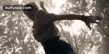 a woman is flying through the air with her arms outstretched in a forest .