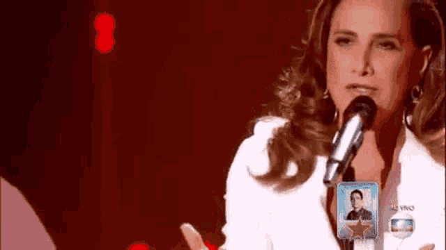 a woman is singing into a microphone with a picture of a man in the background .