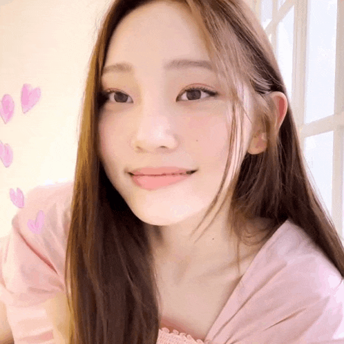 a woman with long brown hair is wearing a pink shirt and smiling