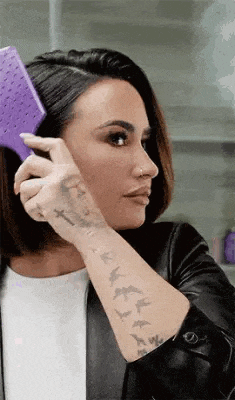 a woman with tattoos is brushing her hair with a purple brush .