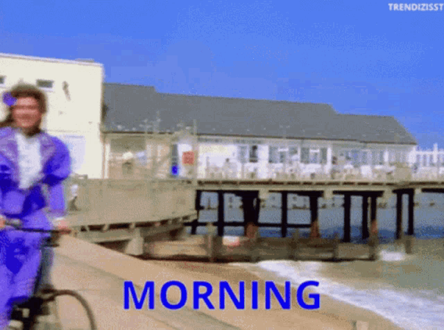 a man in a purple suit is riding a bike on a beach and the words morning are on the bottom