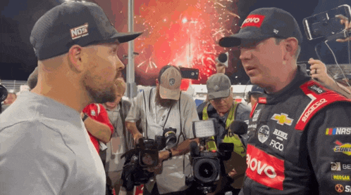 a man wearing a nos hat is talking to another man in a racing uniform