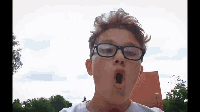a young boy wearing glasses makes a funny face with his mouth open