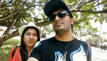 a man wearing sunglasses and a hat stands next to a woman wearing a white hat