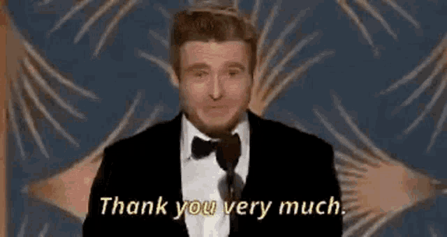 a man in a suit is holding an oscar trophy and saying `` thank you very much '' .