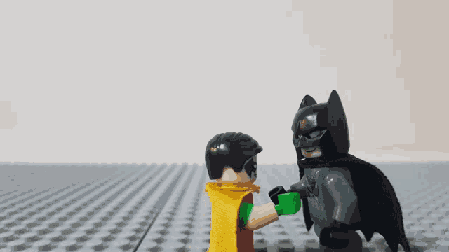 a lego batman and robin are shaking hands on a gray surface