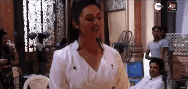 a woman in a white shirt stands in front of a sign that says zee alt