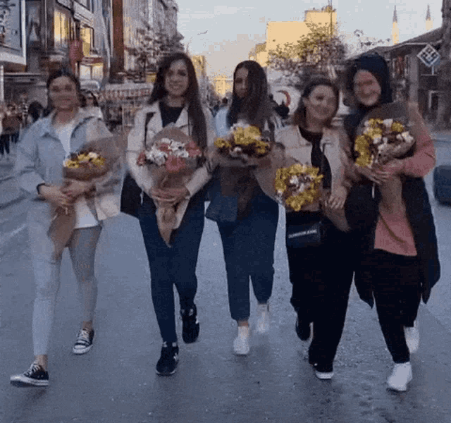 a group of women are walking down a street holding flowers