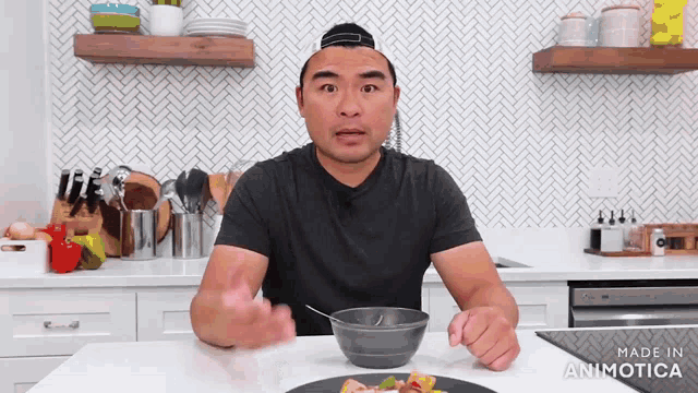 a man in a black shirt is sitting at a table with a bowl of food and the words made in animatica on the bottom right