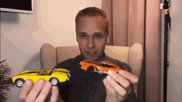 a man is sitting in a chair holding two toy cars .