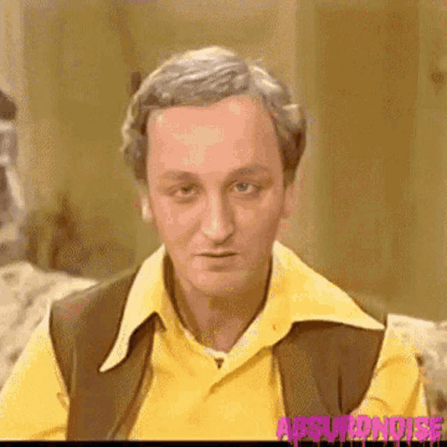 a man wearing a yellow shirt and a brown vest is looking at the camera .