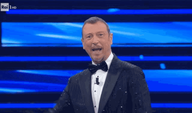 a man in a tuxedo and bow tie stands in front of a rai 1 hd screen